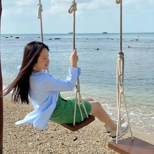 50岁杨钰莹海边度假太惬意,翘腿荡秋千玩心十足,黑发浓密若冻龄